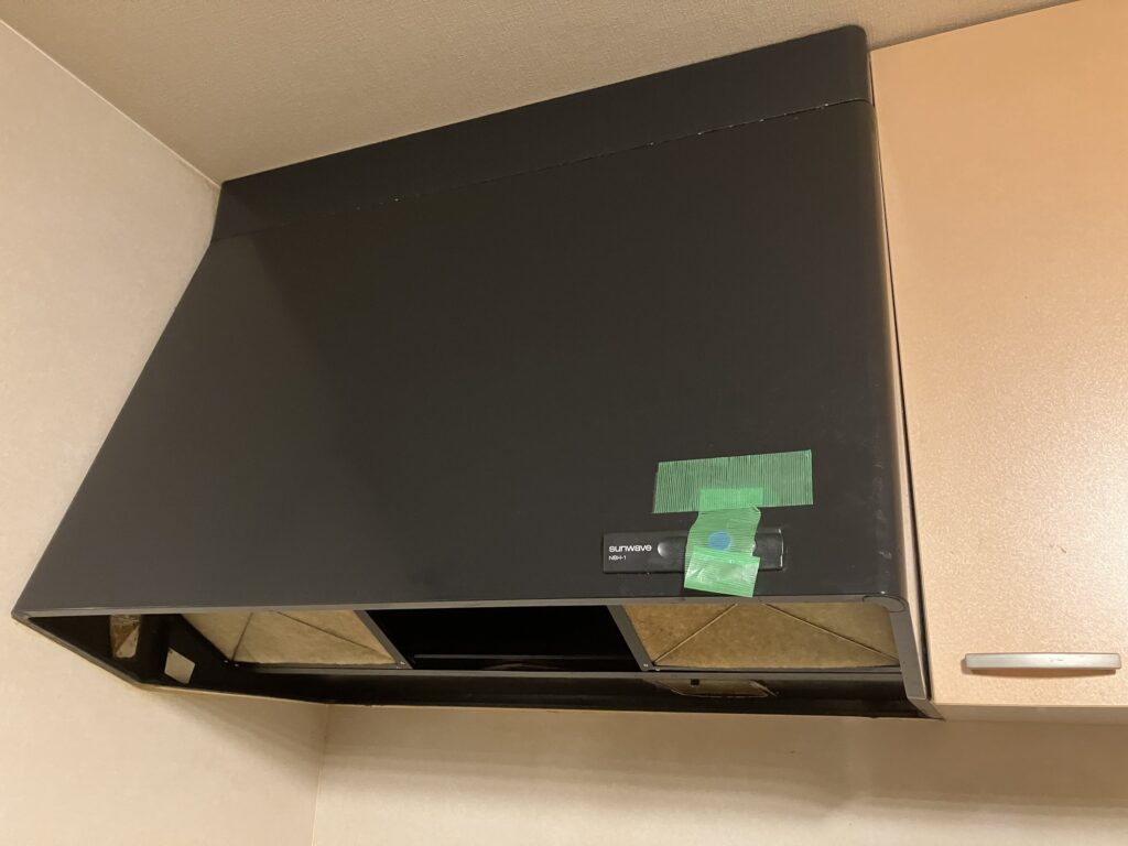 既存のレンジフードは黒色のフード型で、表面に油汚れが目立ち、経年による劣化が見られます。
