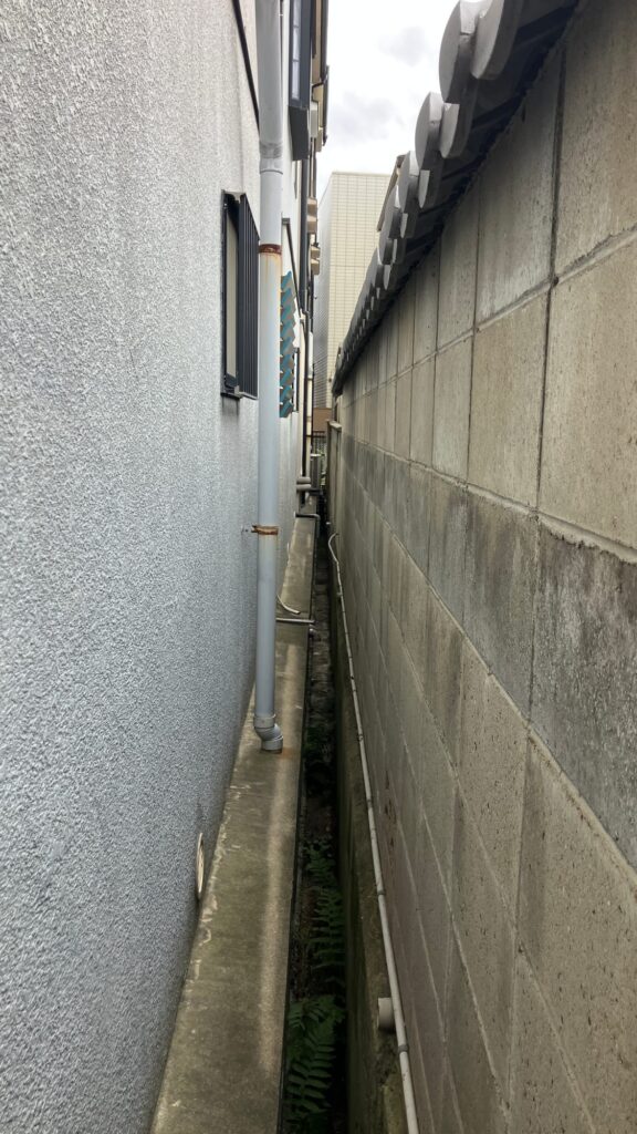建物側面の狭小通路。高圧洗浄や塗装の際、隣地との距離が近く、養生と飛散防止に配慮が必要でした。